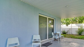 A covered outdoor seating area with white chairs and a table, a sliding glass door, and a concrete floor. - Suntan, Shop & Explore! Seminole Escape (Seminole)