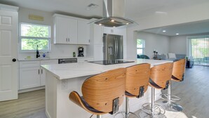 A modern kitchen with white cabinetry, a stainless steel refrigerator, and a central island with bar stools. - Suntan, Shop & Explore! Seminole Escape (Seminole)