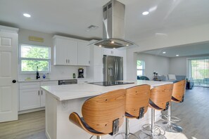 Eine moderne Küche mit weißen Schränken, einem Edelstahlkühlschrank und einer zentralen Kochinsel mit Barhocker.