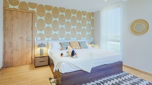 A bedroom with a wooden door, a bed with white bedding, patterned pillows, a bedside lamp, and a large window. - Bonsai 1BR Suite- Yutori 306 (Noord)