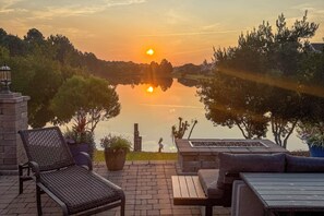 A patio with outdoor furniture, a view of a lake, and a sunset.
