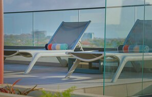 Two lounge chairs with cushions, positioned on a balcony with a glass railing, overlooking a cityscape. - Bonsai 2BR Retreat-Flow 201 (Noord)