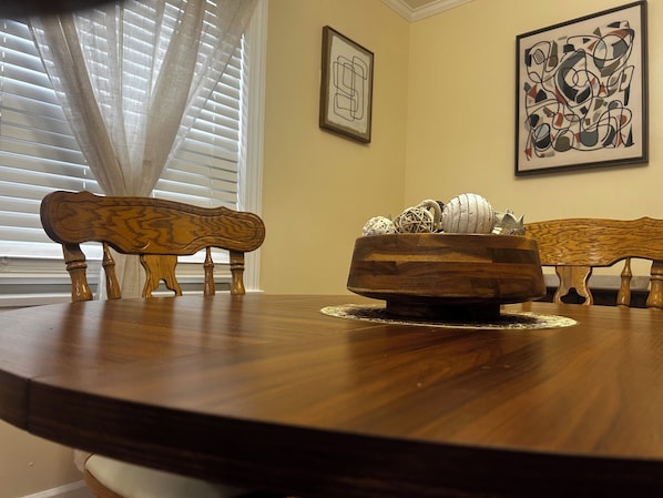 A dining table with a wooden bowl centerpiece, two chairs, and a window with blinds.