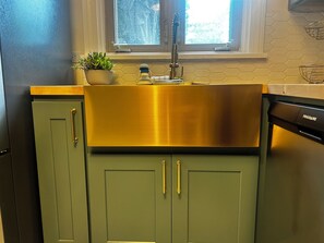A kitchen with a stainless steel sink, green cabinets, and a window above the sink.