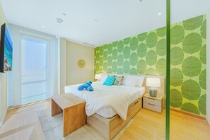A hotel room with a bed, bedside table, lamp, and a view of the sea through a window. - Bonsai 2BR Retreat-Midori 210 (Noord)