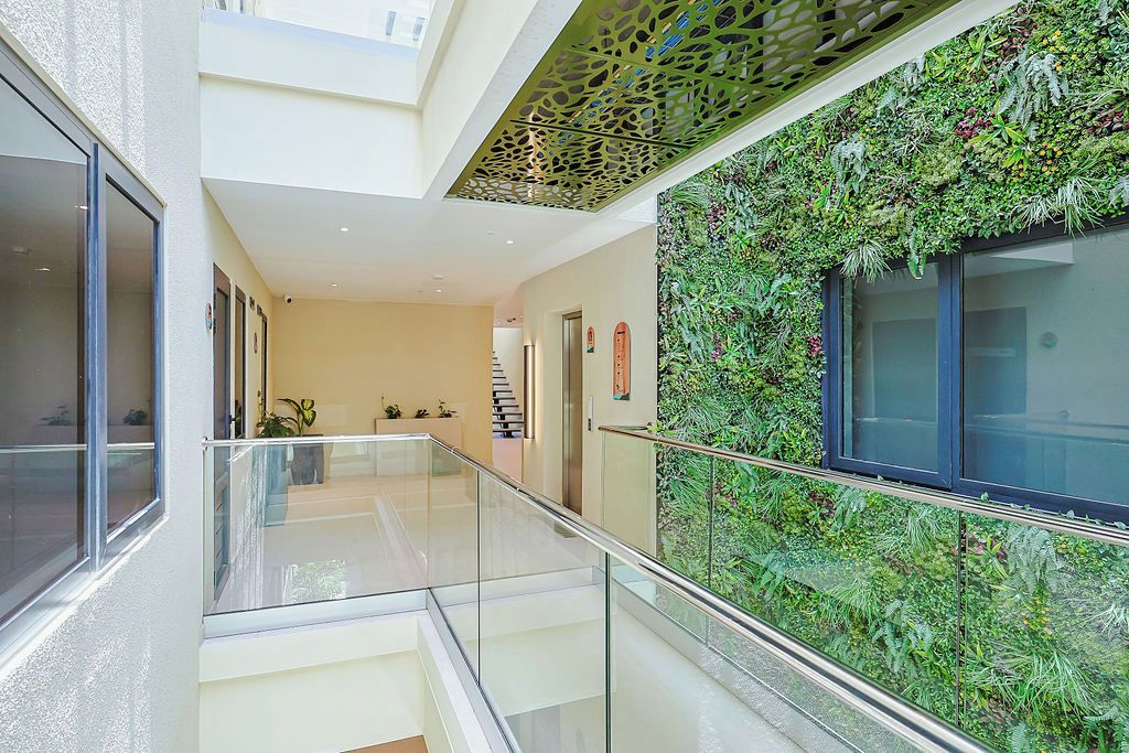 Interior moderno com guarda-corpo de vidro, escada e parede coberta por vegetação.