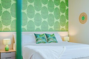 A hotel room with a bed, pillows, a nightstand, a lamp, and a wall with a leaf pattern. - Bonsai 2BR Retreat-Balance 211 (Noord)