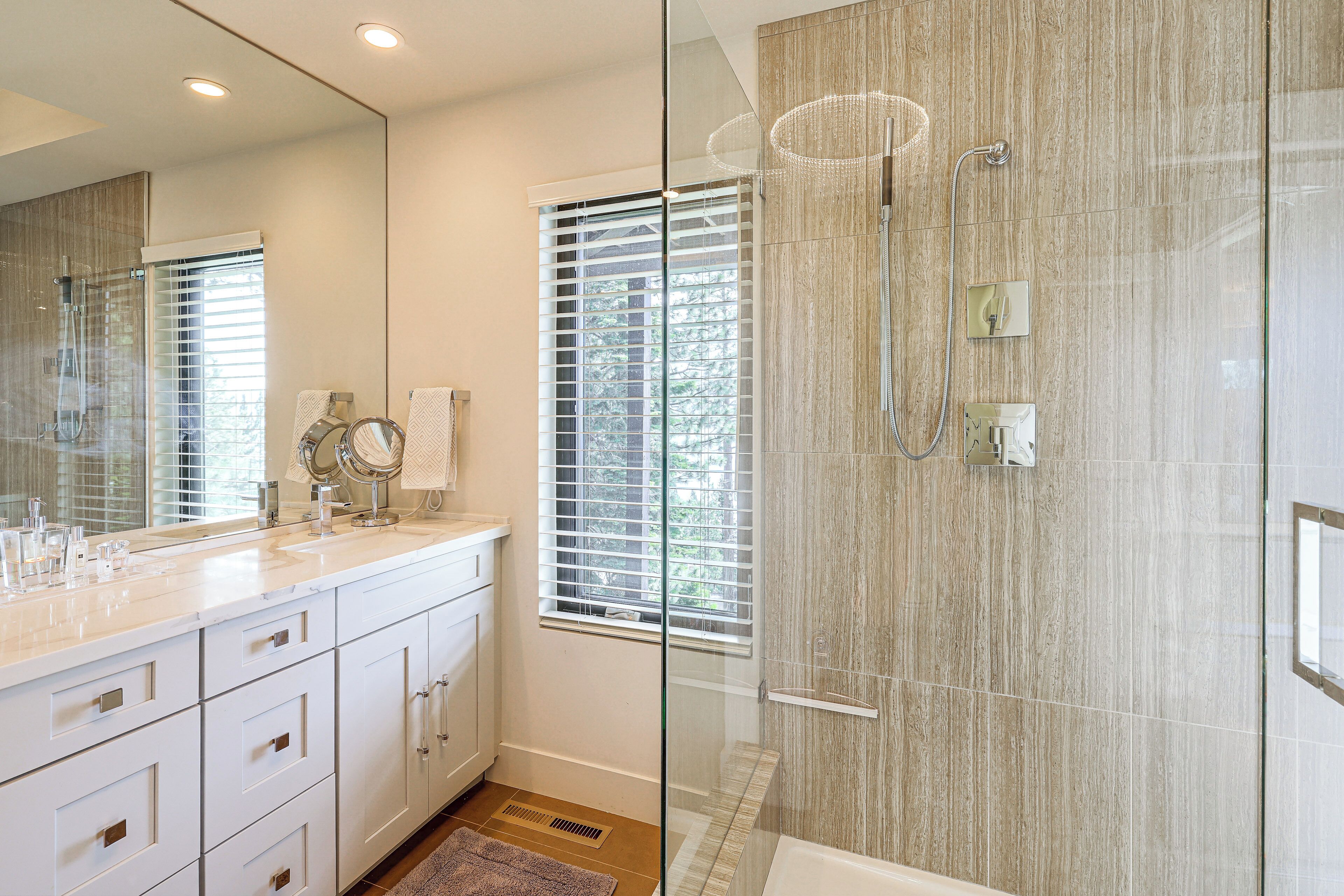 A modern bathroom with a glass shower enclosure, a large mirror, and a vanity with a sink and multiple drawers.