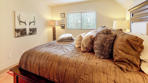 Un dormitorio con una cama grande, una ventana con persianas, una lámpara de pared y un cuadro.
