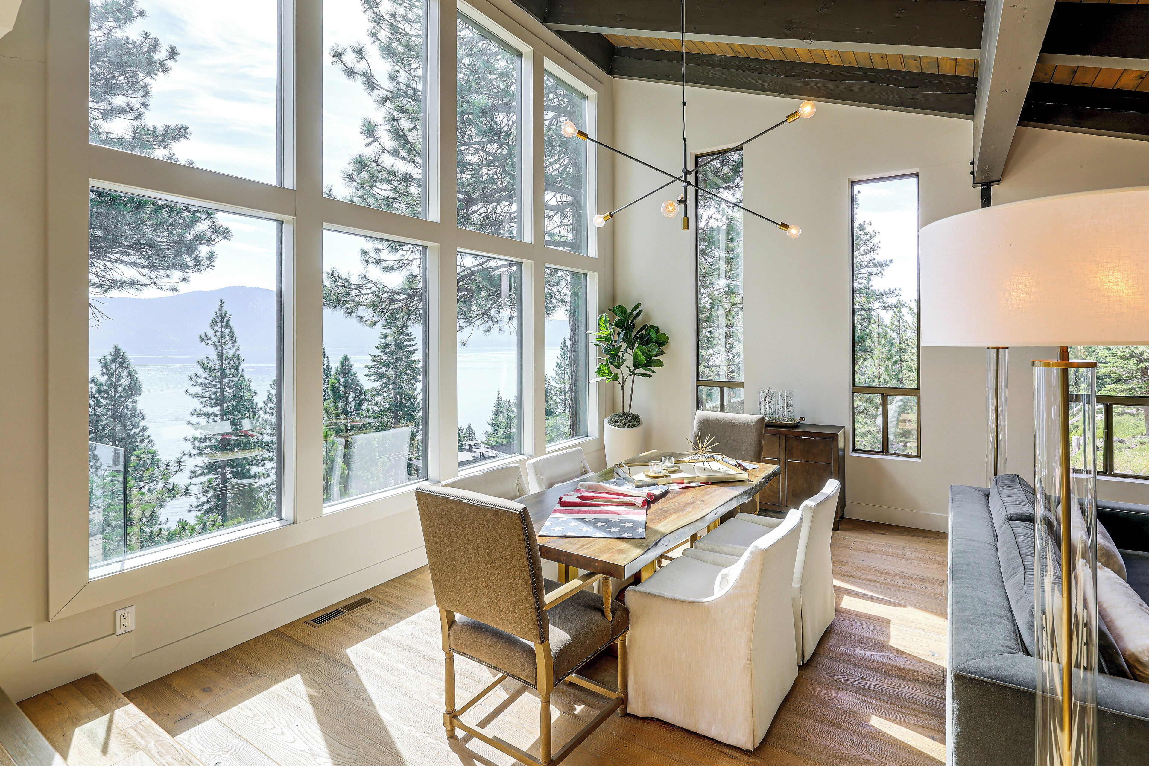 A spacious room with large windows offering a view of a lake and trees, a dining table with chairs, and a sofa.