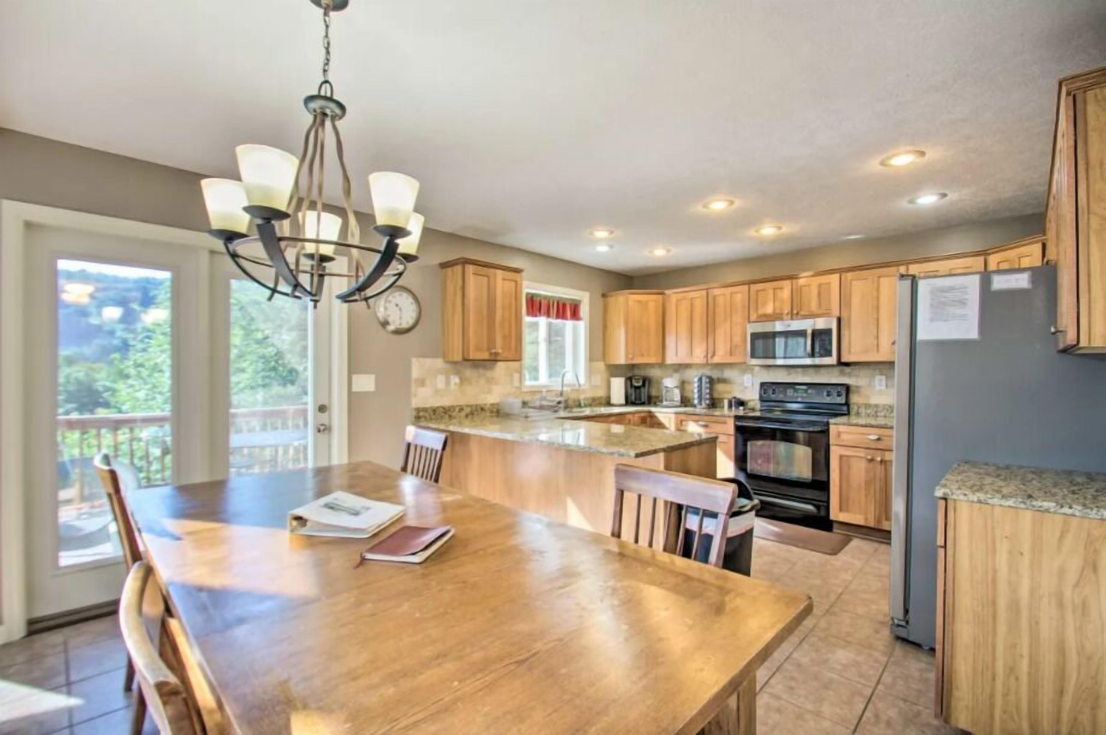 A kitchen with wooden cabinets, a granite countertop, a chandelier, and a dining area with a table and chairs.