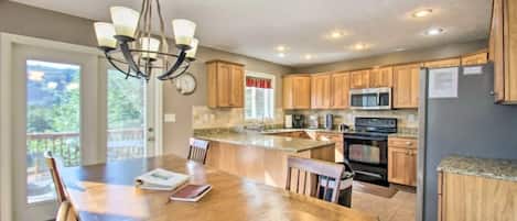 A kitchen with wooden cabinets, a granite countertop, a chandelier, and a dining area with a table and chairs.