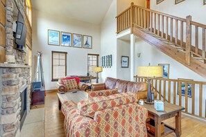A spacious living room with a fireplace, a leather sofa, a wooden coffee table, and a staircase. - Hike, Bike & Ski! Rendezvous Cabin w/ Mtn Views (Fraser)