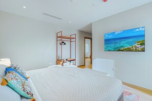 A modern bedroom with a bed, a TV on the wall, and a view of the sea. - Bonsai 2BR Retreat-Red Bloom 310 (Noord)