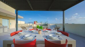 A rooftop dining area with a table set for six, surrounded by red chairs, under a clear sky. - Bonsai 2BR Retreat-Sora 311 (Noord)