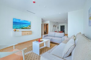 Ein modernes Wohnzimmer mit Fernseher, grauem Sofa, weißem Couchtisch und Holzboden.