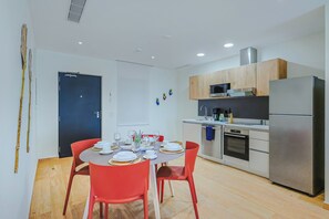 Eine moderne Küche mit Essbereich, ausgestattet mit Kühlschrank, Mikrowelle, Backofen und einem Esstisch, der mit Tellern und Gläsern gedeckt ist.