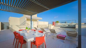 Una terrazza sul tetto con un tavolo da pranzo per quattro persone, circondata da sedie rosse e una panca rossa.