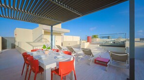 A rooftop terrace with a dining table set for four, surrounded by red chairs, and a red bench. - Bonsai 3BR Retreat Grand 207 (Noord)