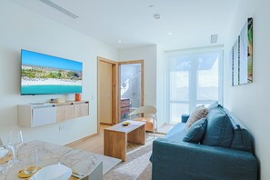 A modern living room with a television, a sofa, and a dining area with a table and chairs. - Bonsai 3BR Retreat Grand 207 (Noord)