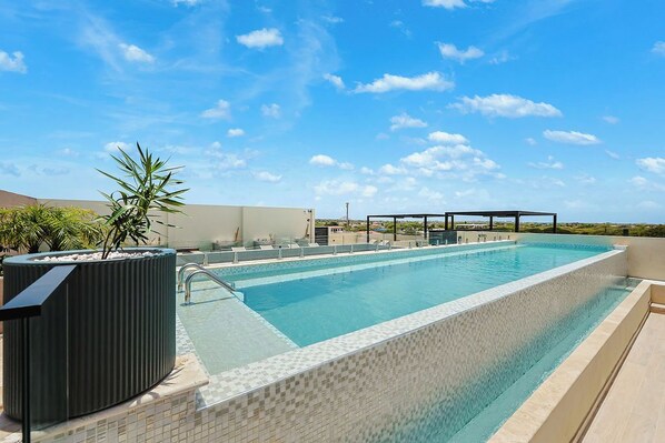 A rooftop infinity pool with a clear view of the horizon, surrounded by lounge chairs and a pergola. - Bonsai 3BR Retreat Grand 207 (Noord)