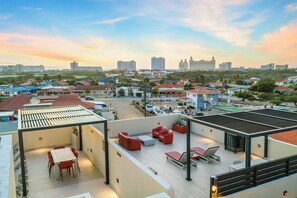 A rooftop terrace with outdoor seating, a view of the cityscape, and a clear sky. - Bonsai 3BR Retreat Grand 207 (Noord)