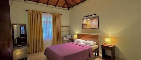 A bedroom with a bed, bedside tables, a mirror, curtains, and a painting on the wall.