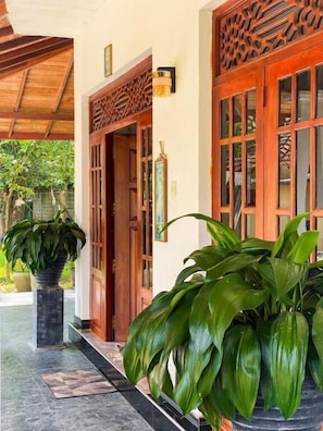 A building entrance with a wooden door, a potted plant, and a wall-mounted light fixture.