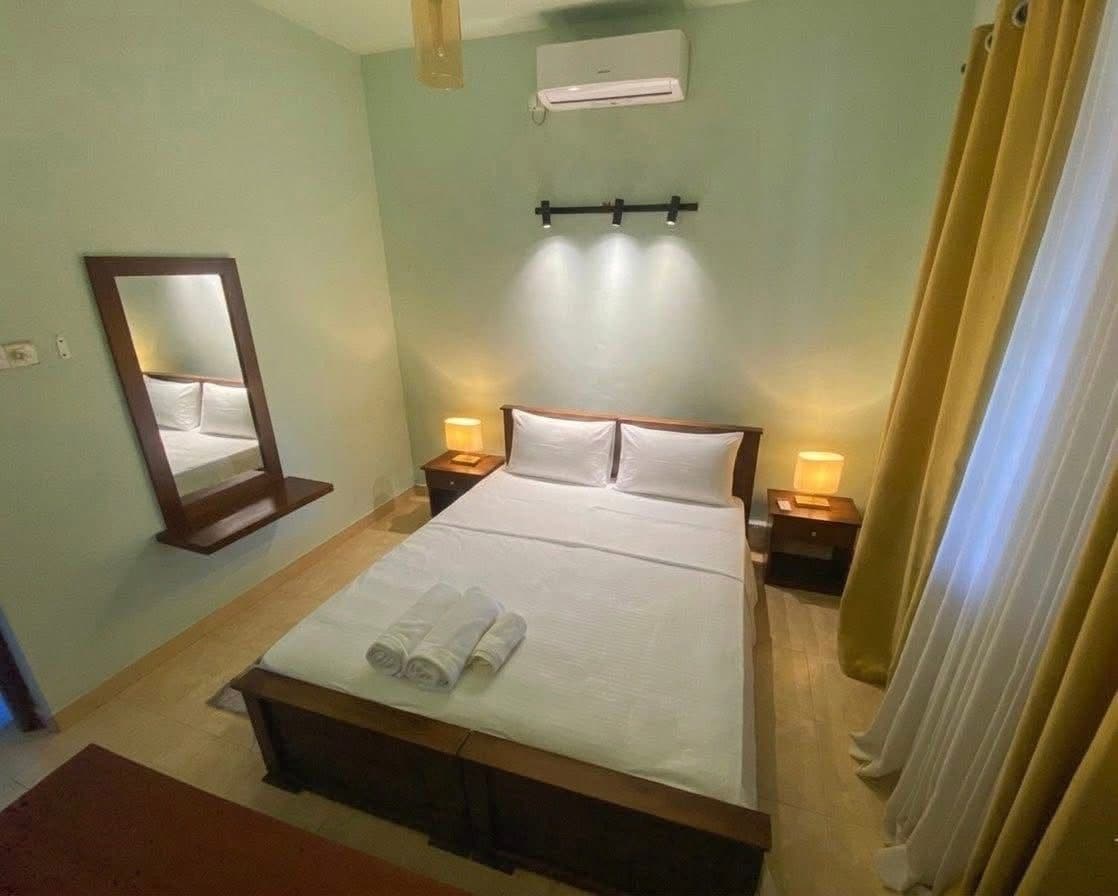 A hotel room with a bed, bedside lamps, a mirror, and an air conditioning unit.