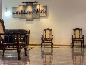 Ein Zimmer mit Stadtbild-Kunstwerk, zwei Holzstühlen und einem Ledersofa.