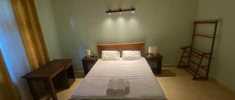 Un dormitorio con una cama de madera, mesitas de noche, un archivador y un estante en la pared.