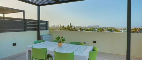 An outdoor patio with a table and chairs, a potted plant, and a view of a cityscape.