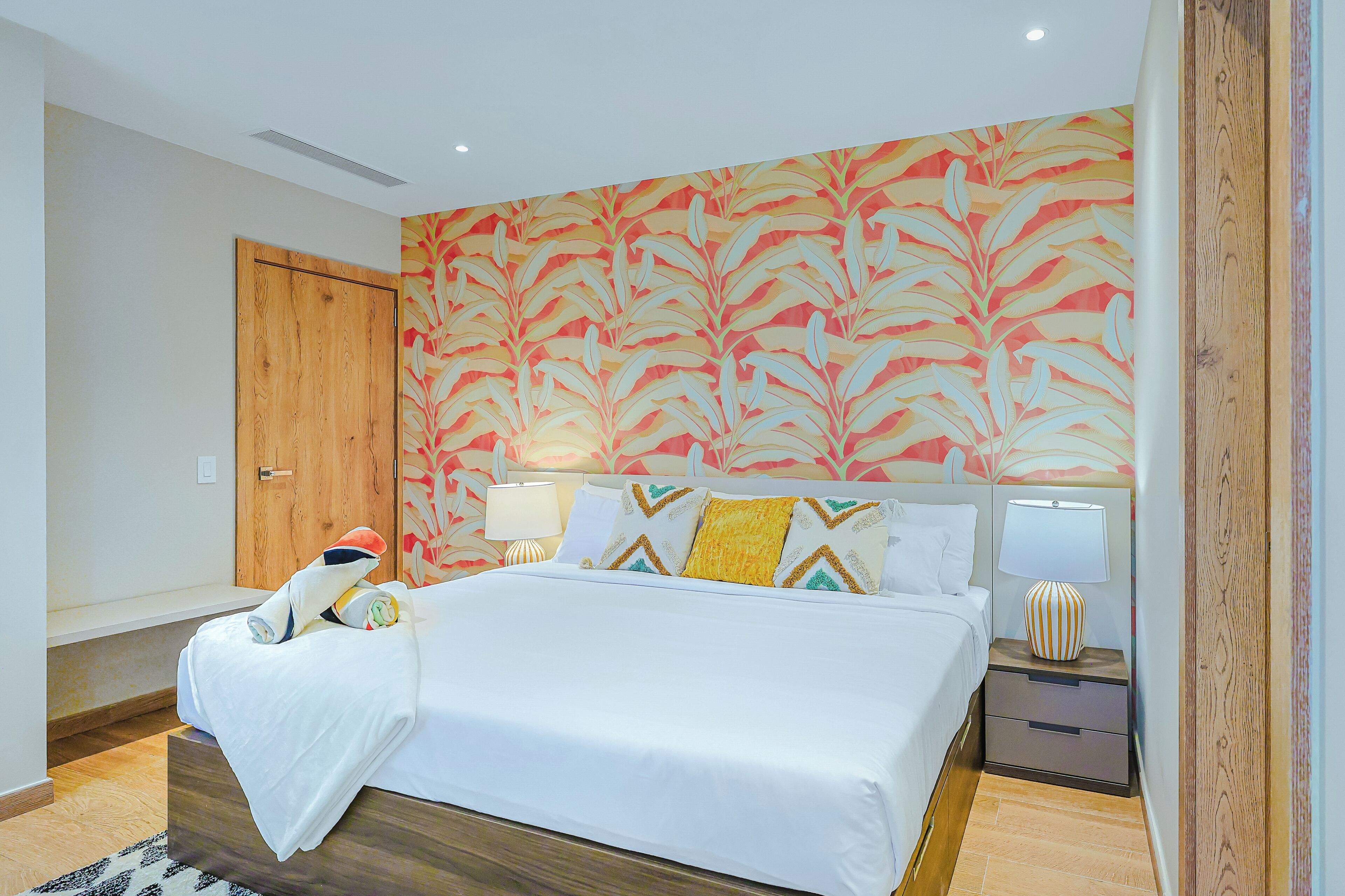 Une chambre d’hôtel avec un lit, deux lampes de chevet, une porte en bois et un mur orné d’un motif de feuilles.