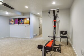 Ein Heimfitnessraum mit einem stationären Fahrrad, einer Hantelbank und einem an der Wand befestigten Trainingsgerät.