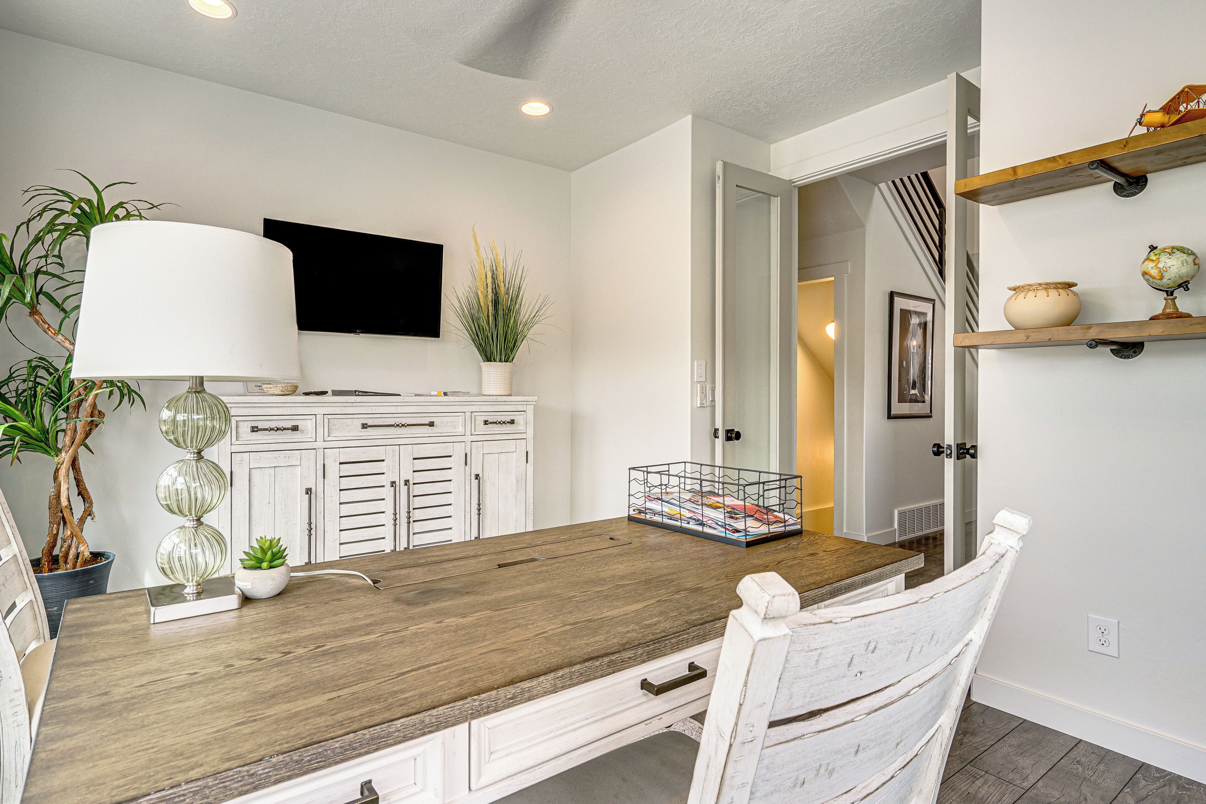 A dining area with a wooden table, white cabinets, a potted plant, and a television on the wall.