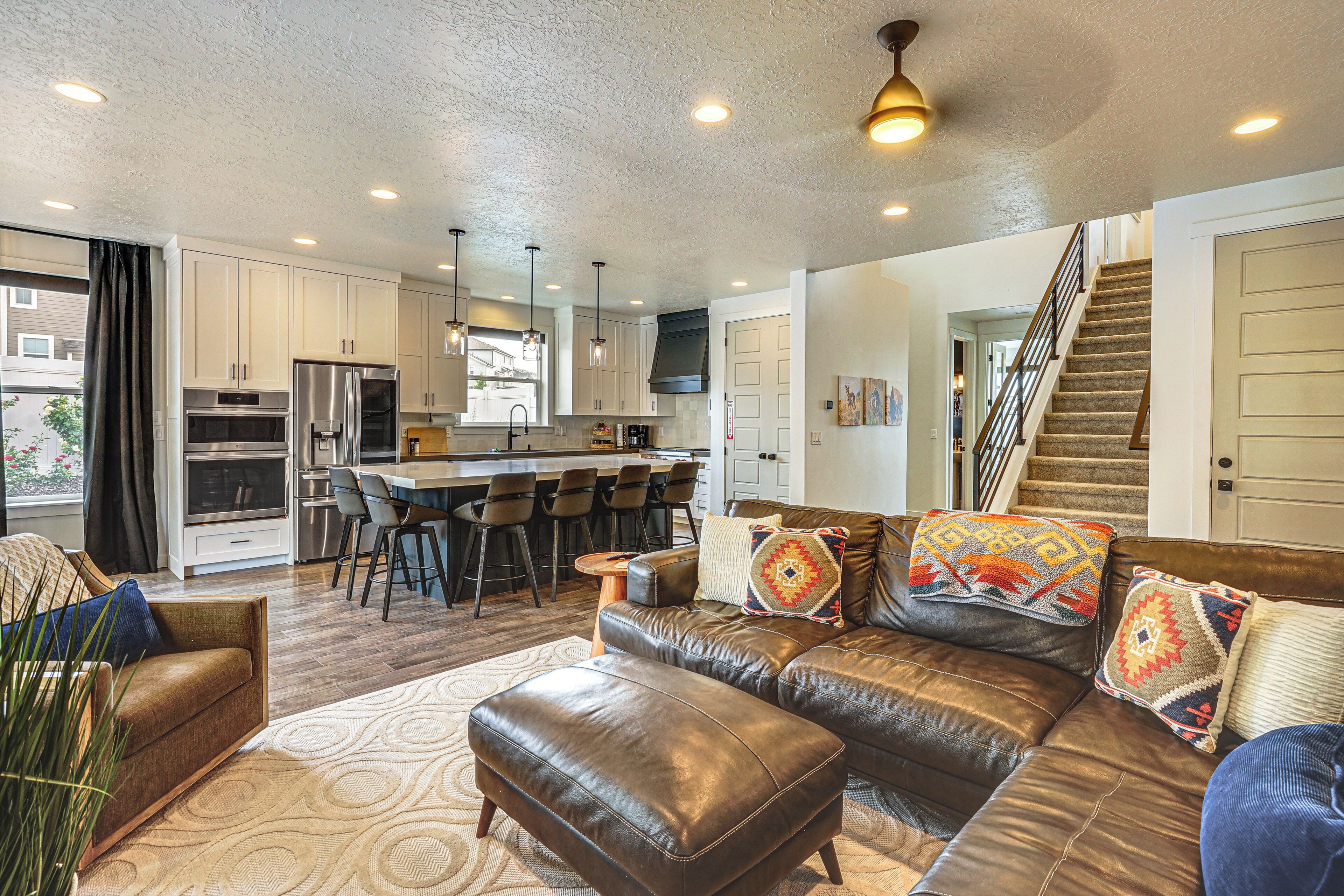 A modern living room with a leather sofa, ottoman, and a dining area with bar stools.