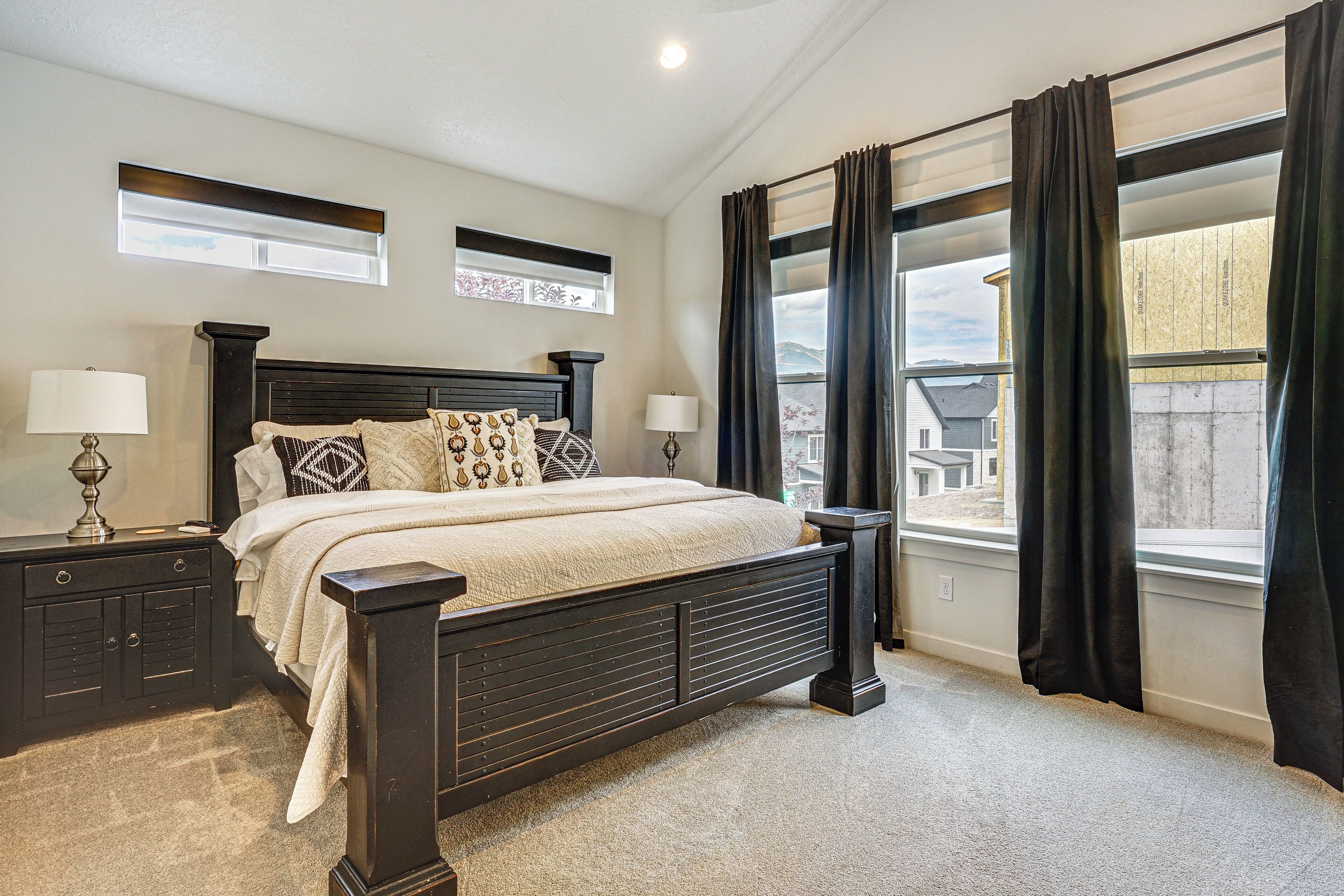 A bedroom with a large bed, two bedside tables, a window with curtains, and a view of a building outside.