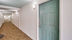 Ein Hotelkorridor mit Teppichböden, weißen Wänden und Türen, wobei rechts eine hellgrüne Tür zu sehen ist.