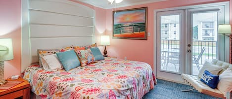 Ein Schlafzimmer mit einem Bett, einem Nachttisch, einer Lampe, einem Deckenventilator, einem Gemälde und Blick ins Freie durch eine Tür.