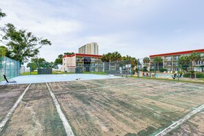En tennisbana med nät, omgiven av ett staket, och belägen intill en byggnad med flera balkonger.