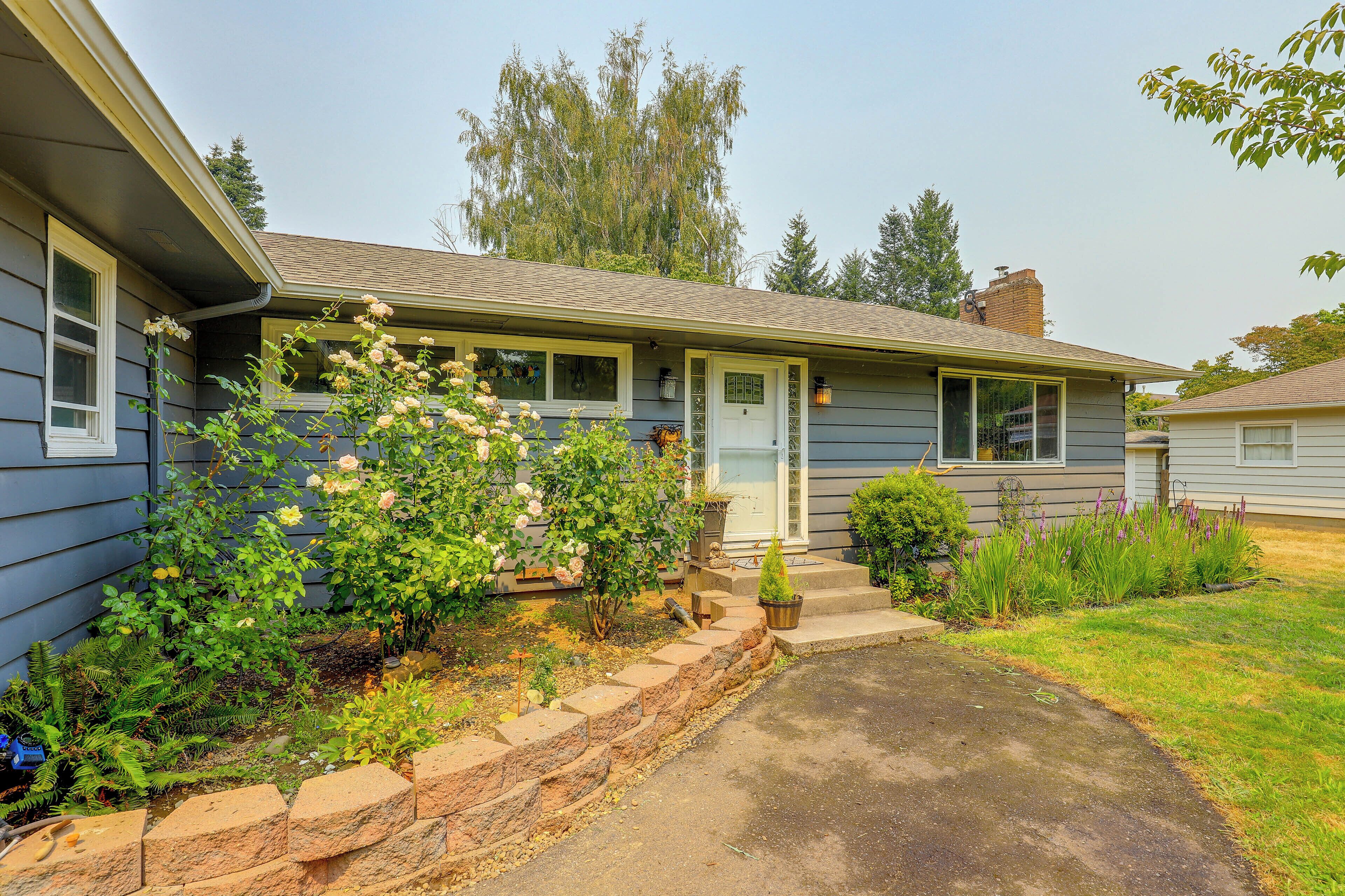 A residential house with a front porch, a small garden with flowering plants, and a clear sky.