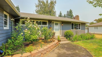 A residential house with a front porch, a small garden with flowering plants, and a clear sky.