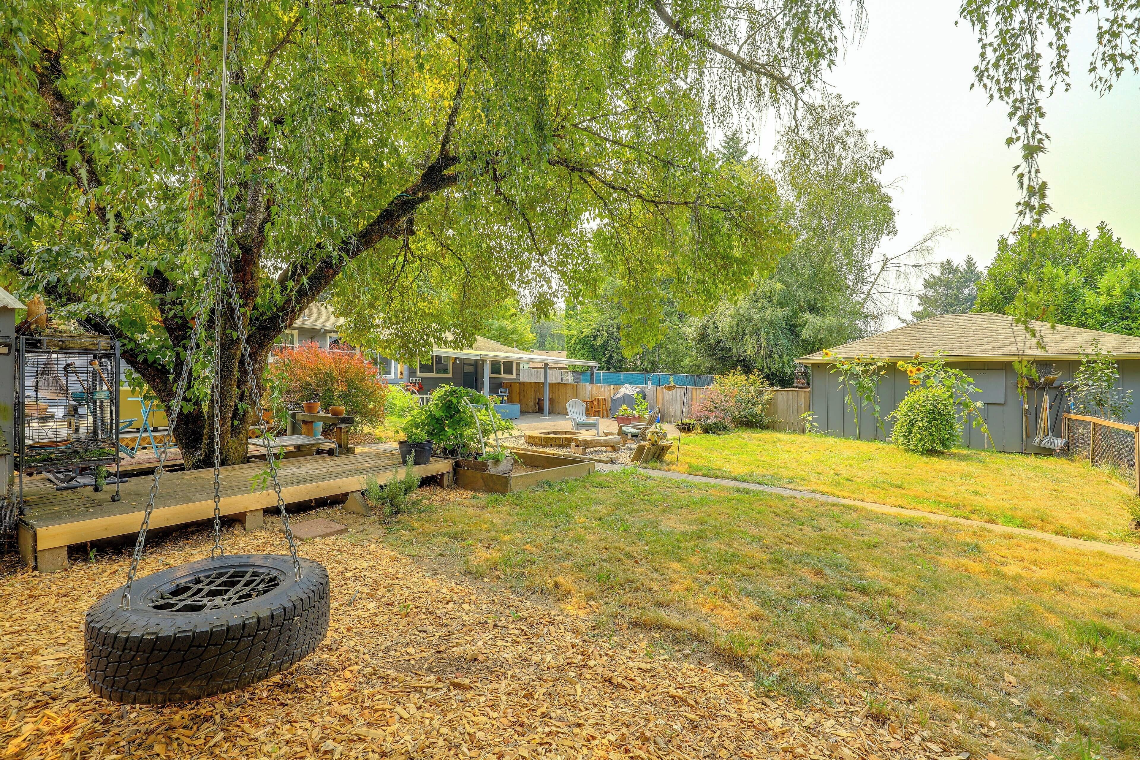 A backyard with a tire swing, a wooden deck, and a fenced area with a house in the background.