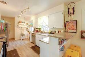 Une cuisine avec des meubles blancs, un îlot central, un réfrigérateur et un coin repas avec une chaise jaune.