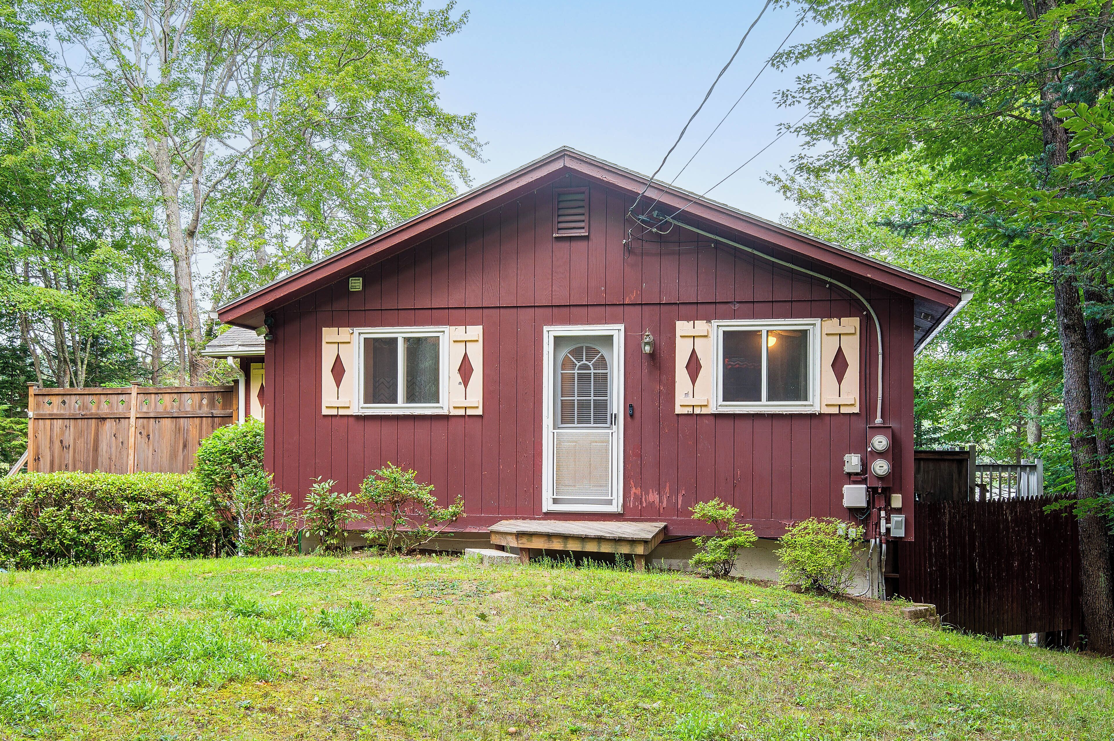 A single-story house with a red exterior, a front door, two windows with shutters, and a small porch.