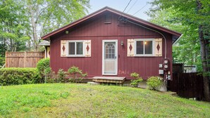 A single-story house with a red exterior, a front door, two windows with shutters, and a small porch. - Lakefront Family Home w/ Docks in Barnstead! (Center Barnstead)