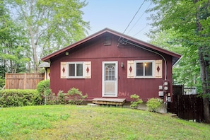 A single-story house with a red exterior, a front door, two windows with shutters, and a small porch.