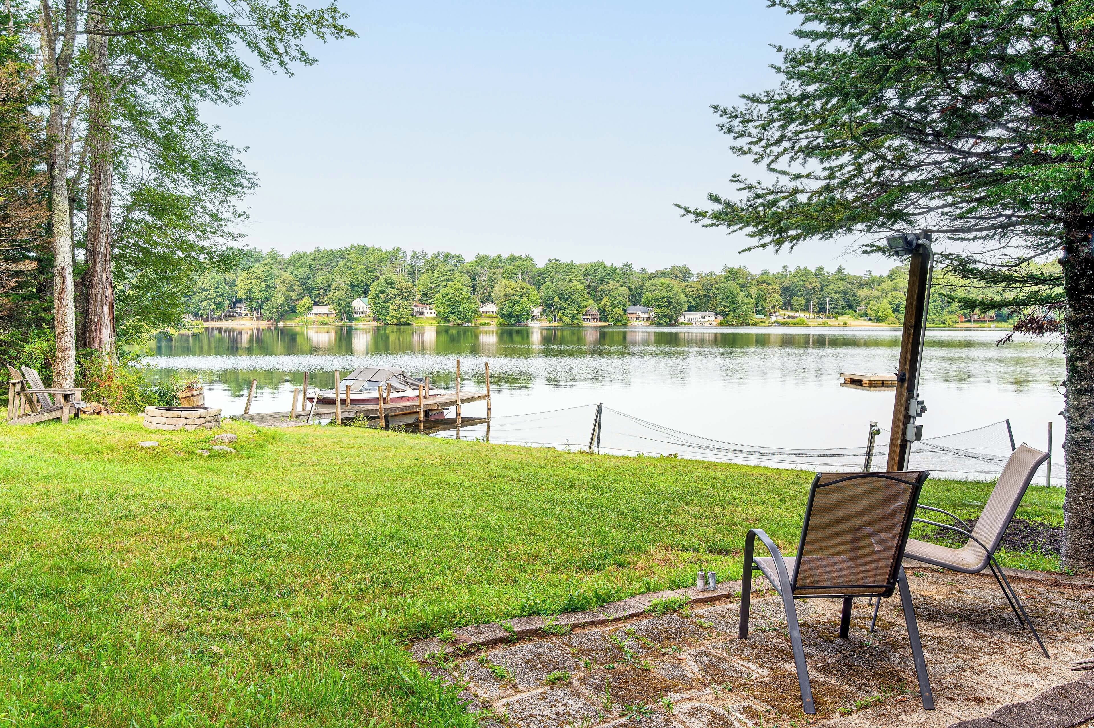 A lakeside view with a dock, chairs, and a chair on the grass.