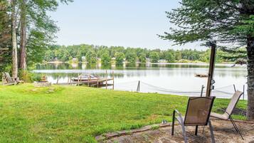 A lakeside view with a dock, chairs, and a chair on the grass.