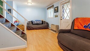 A living room with a staircase, a couch, a radiator, and a door with a window. - Lakefront Family Home w/ Docks in Barnstead! (Center Barnstead)
